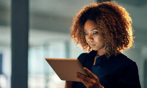 Woman with curly brown hair and a navy blue blouse holding an iPad.
