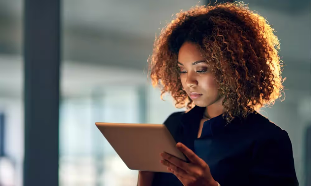 Woman with curly brown hair and a navy blue blouse holding an iPad.