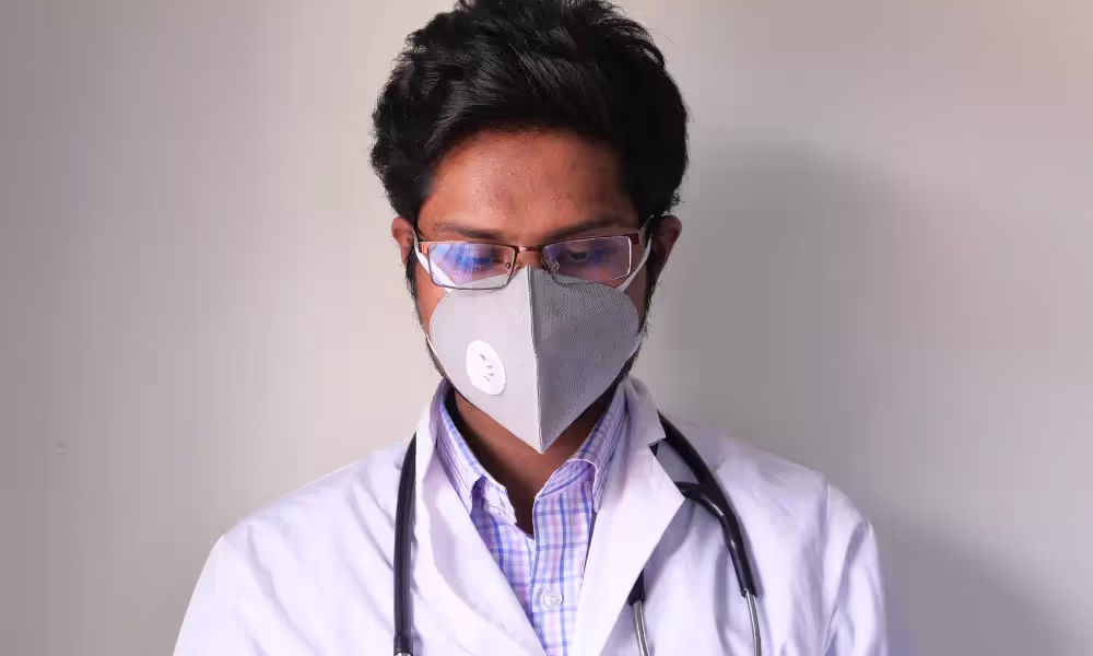 Male doctor wearing a mask and stethescope looking down.