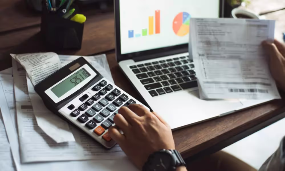 Person holding a calculator on top of a table full of papers with graphs.