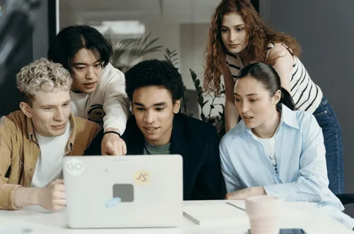Group of coworkers hovering over a laptop.