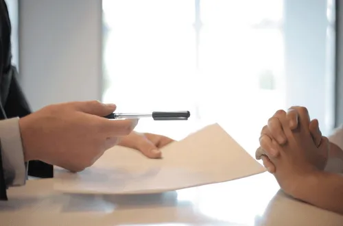 Image of two sets of hands one handing over paper and a pen.