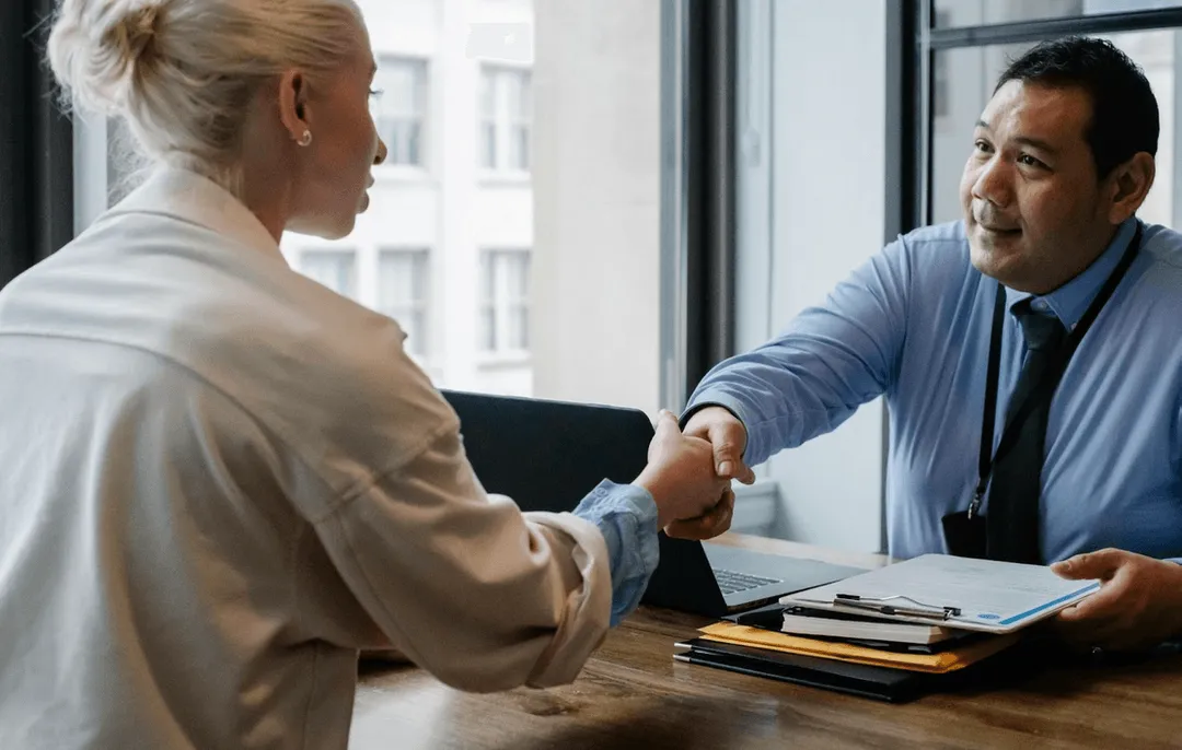 Two people shaking hands over a desk.