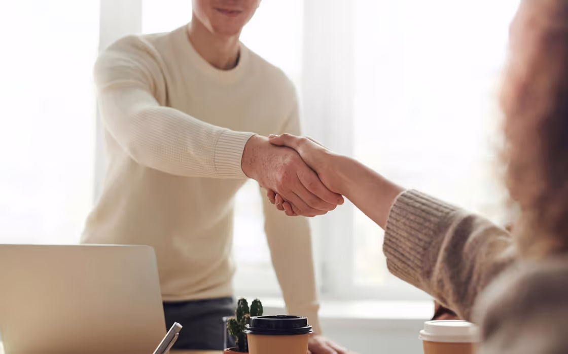 Two people shaking hands over a desk.