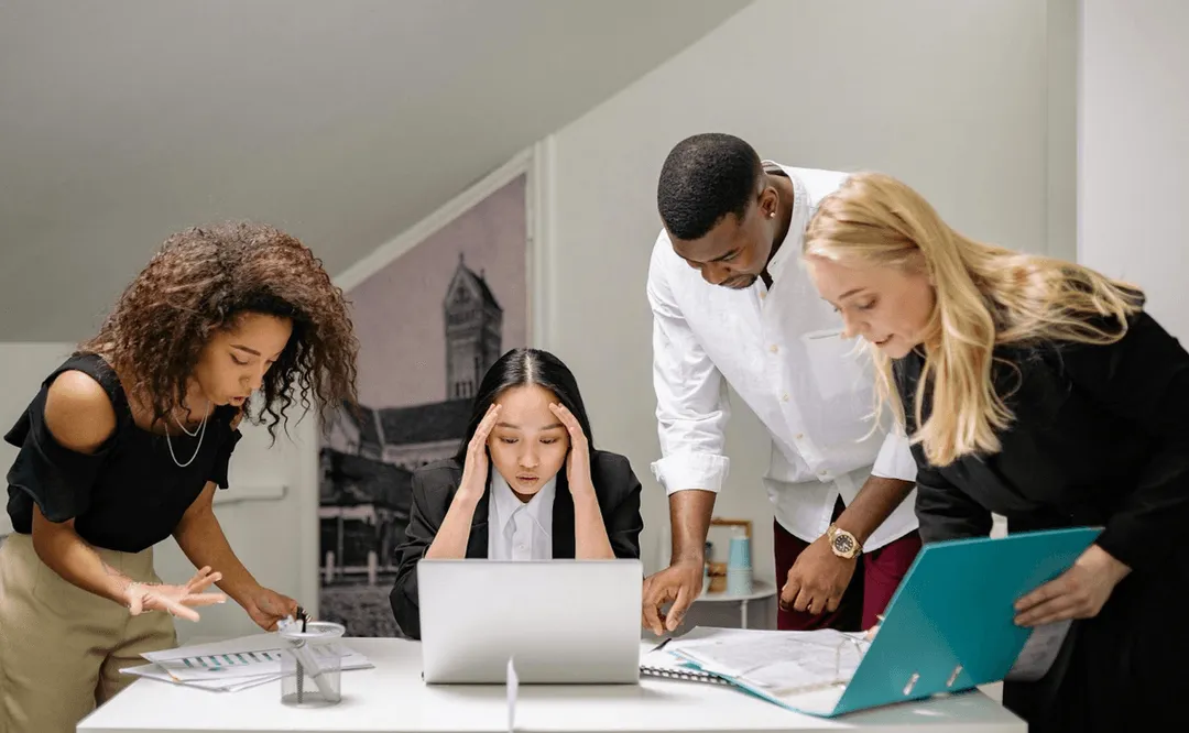 A photo of people gathered around a desk looking stressed.