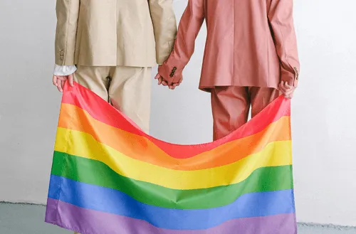 Backside of two people holding hands and the pride flag.