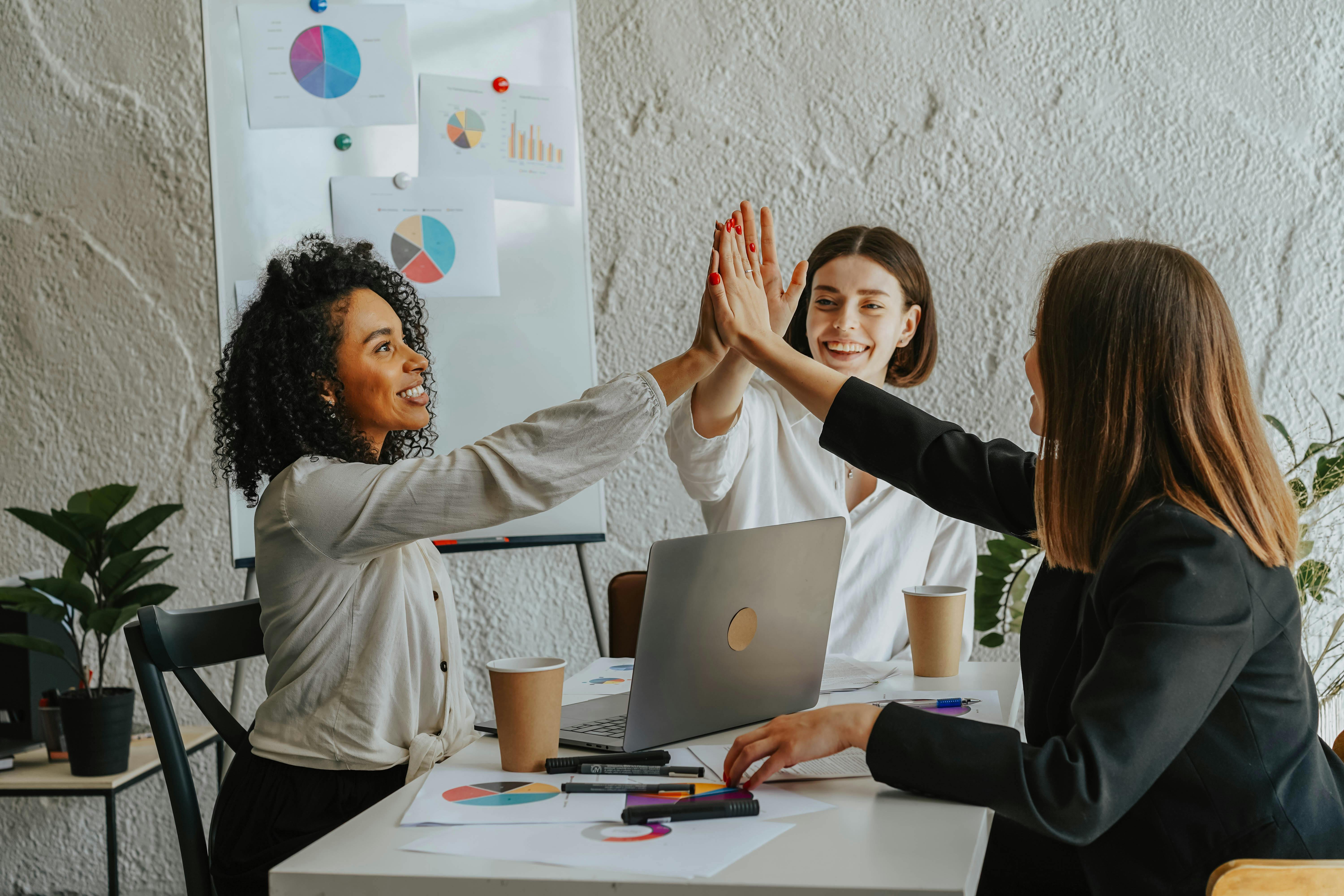Three coworkers in the office join hands in a high five.