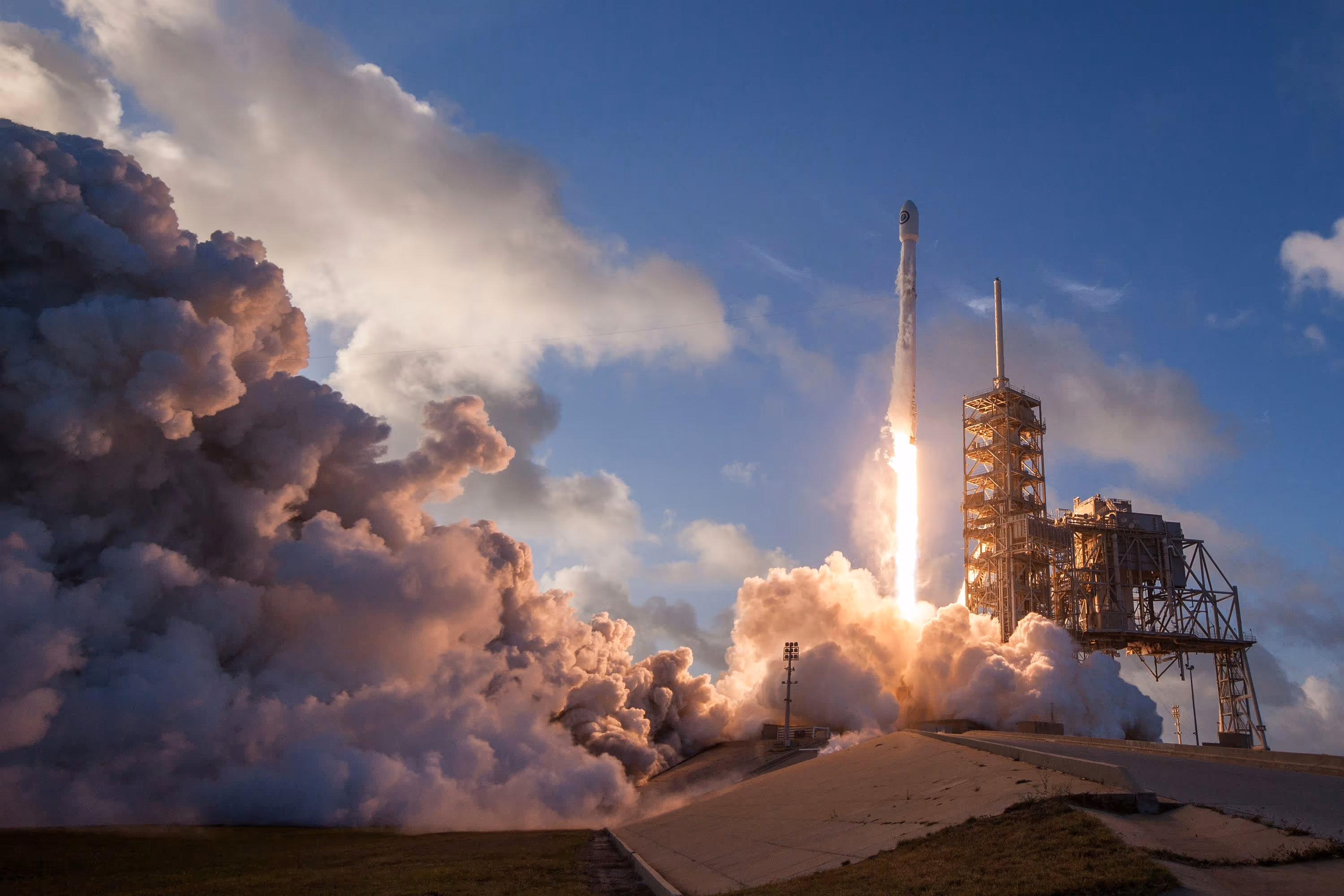 Rocket launching from a launchpad with large clouds of smoke and bright flame against a blue sky.