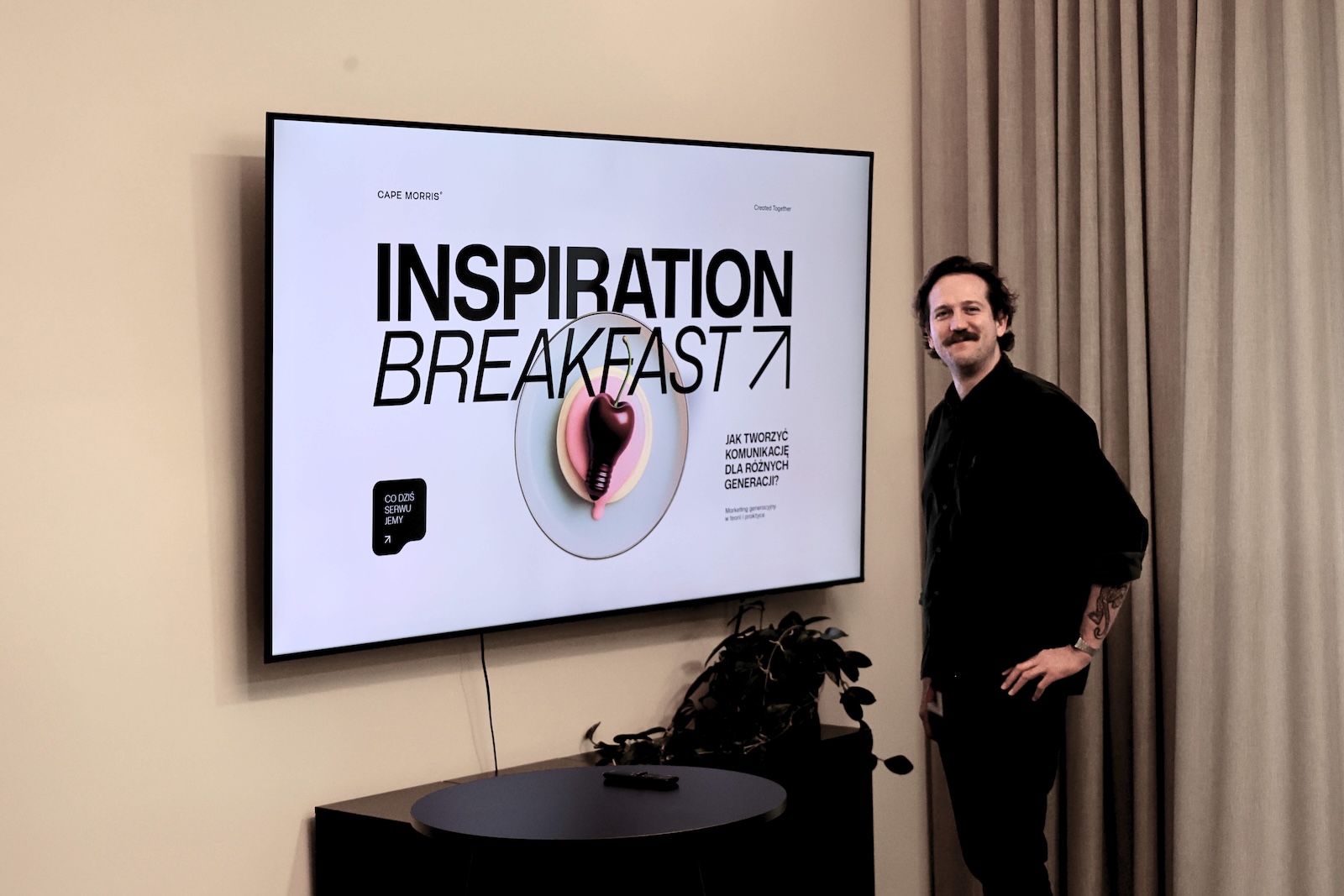 Zdjęcie przedstawia jednego z prowadzących Krzysztofa który pozauje przy ekranie na którym wyświetla się logo i nazwa wydarzenia.