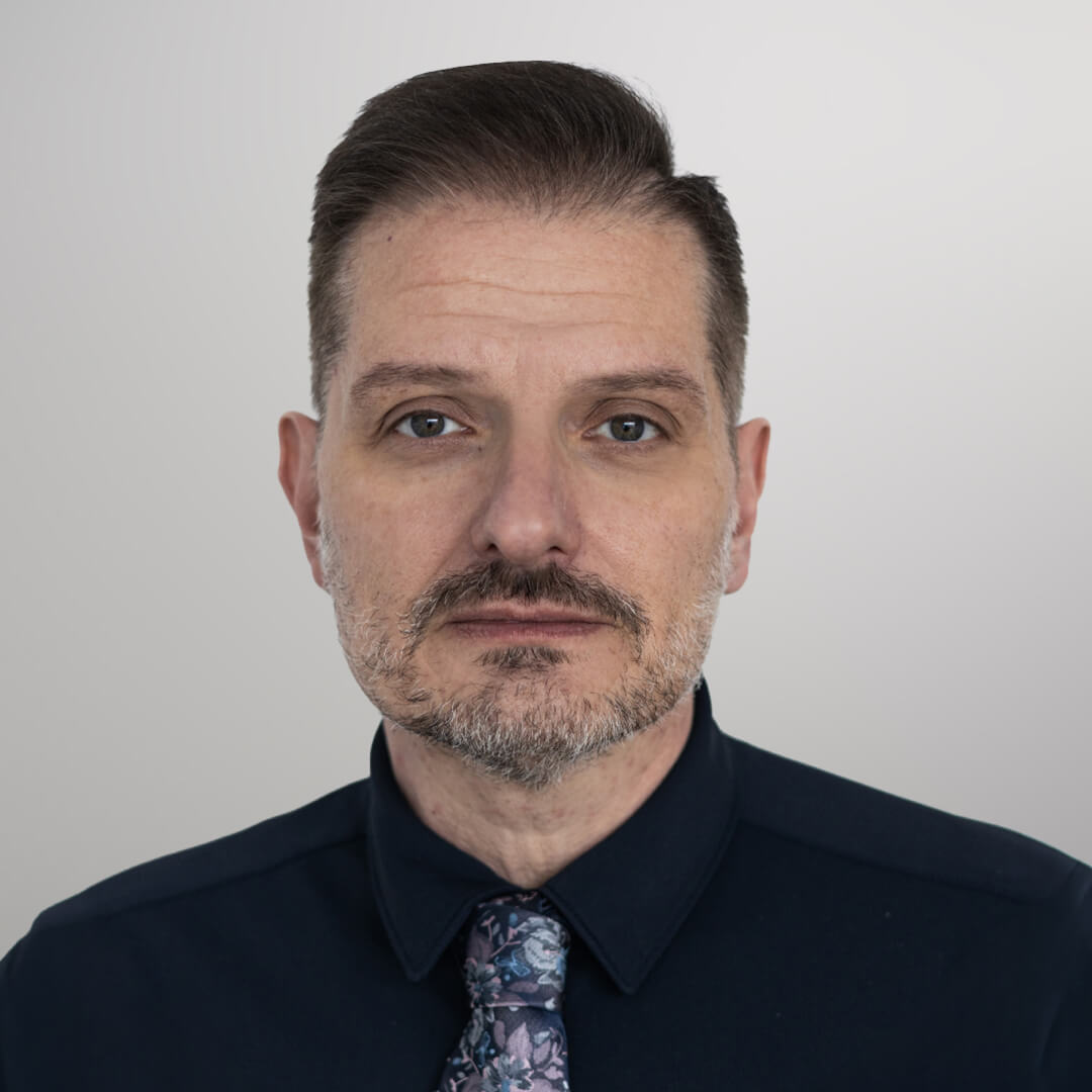 Zdjęcie przedstawia osobę odpowiedzialną za kontakt z uczestnikami oraz jednego z prowadzących Krzysztofa Żukowskiego. Krzysztof siedzi przy stole a na jego kolanach znajduje się nasz Senior Good Boy, piesek Stefan.