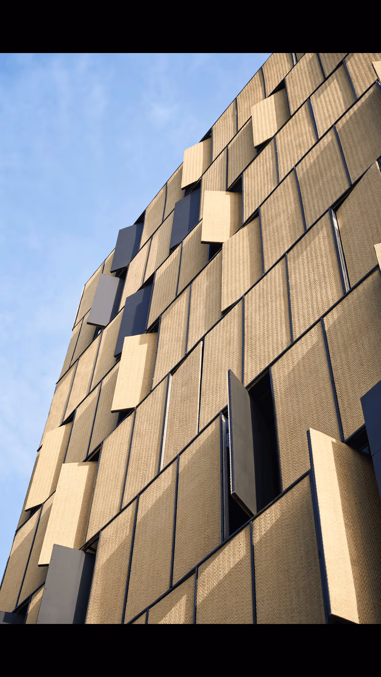 Фасада на сграда с повдигащи се златисти панели, с небето на заден план.