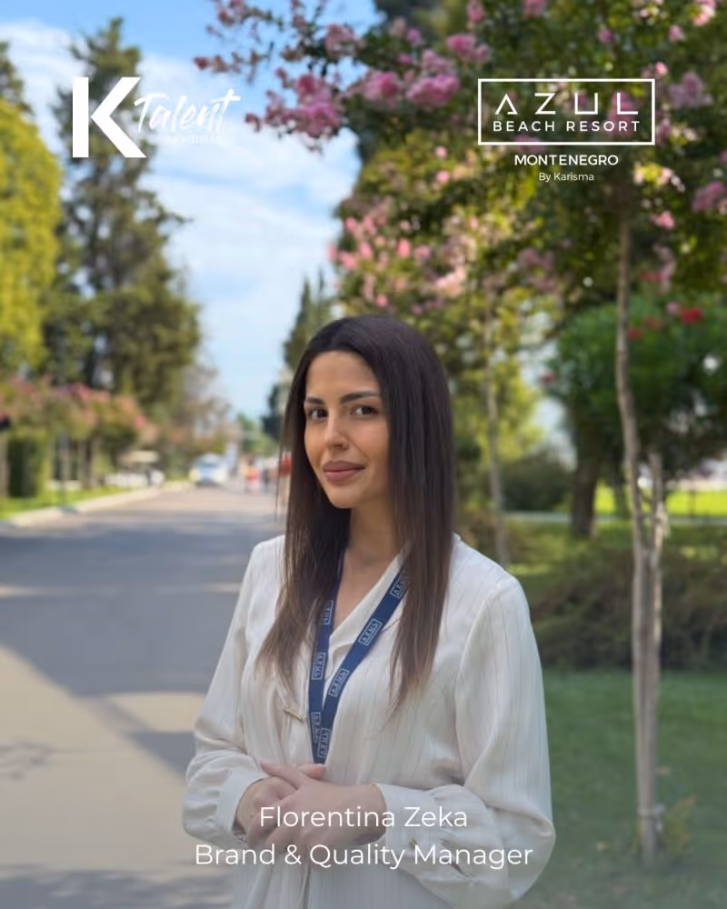Florentina Zeka, a woman with long dark hair wearing a white blouse and an Azul Beach Resort lanyard, standing outdoors with trees and flowers in the background.