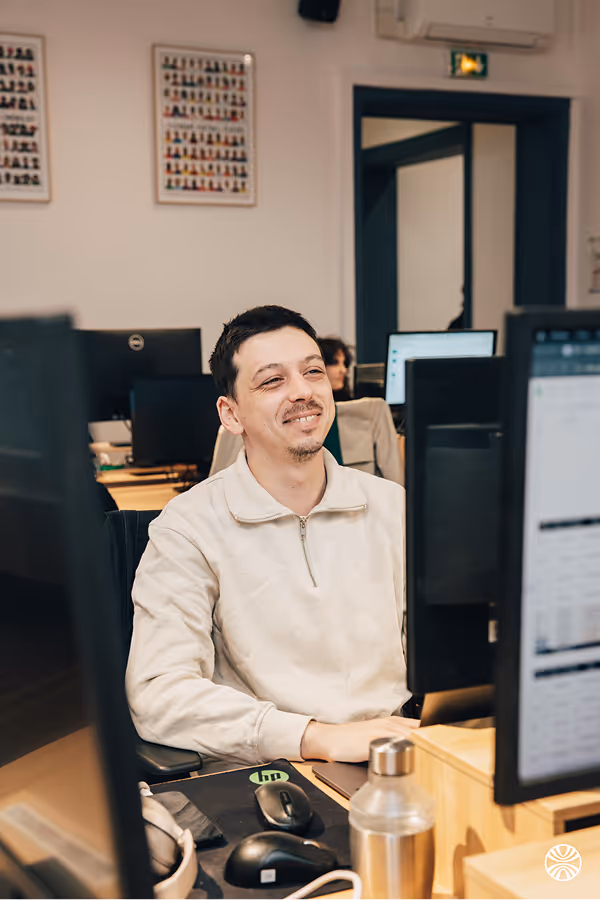 Homme souriant assis à un bureau devant un ordinateur dans un bureau moderne.