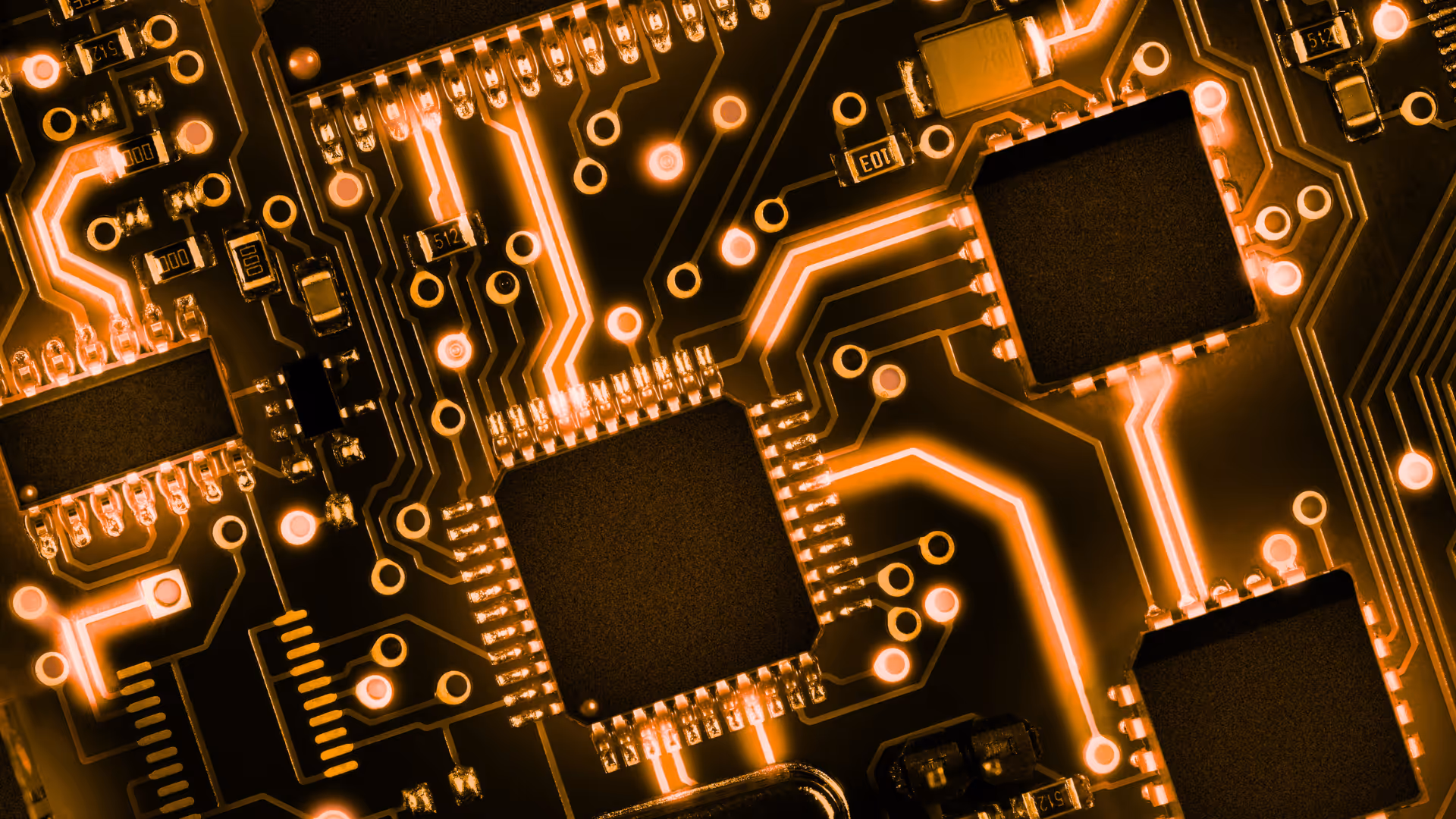 Office desk with a closed silver laptop, an orange figurine with outstretched arms, eyeglasses, orange pen, and some papers by a window.