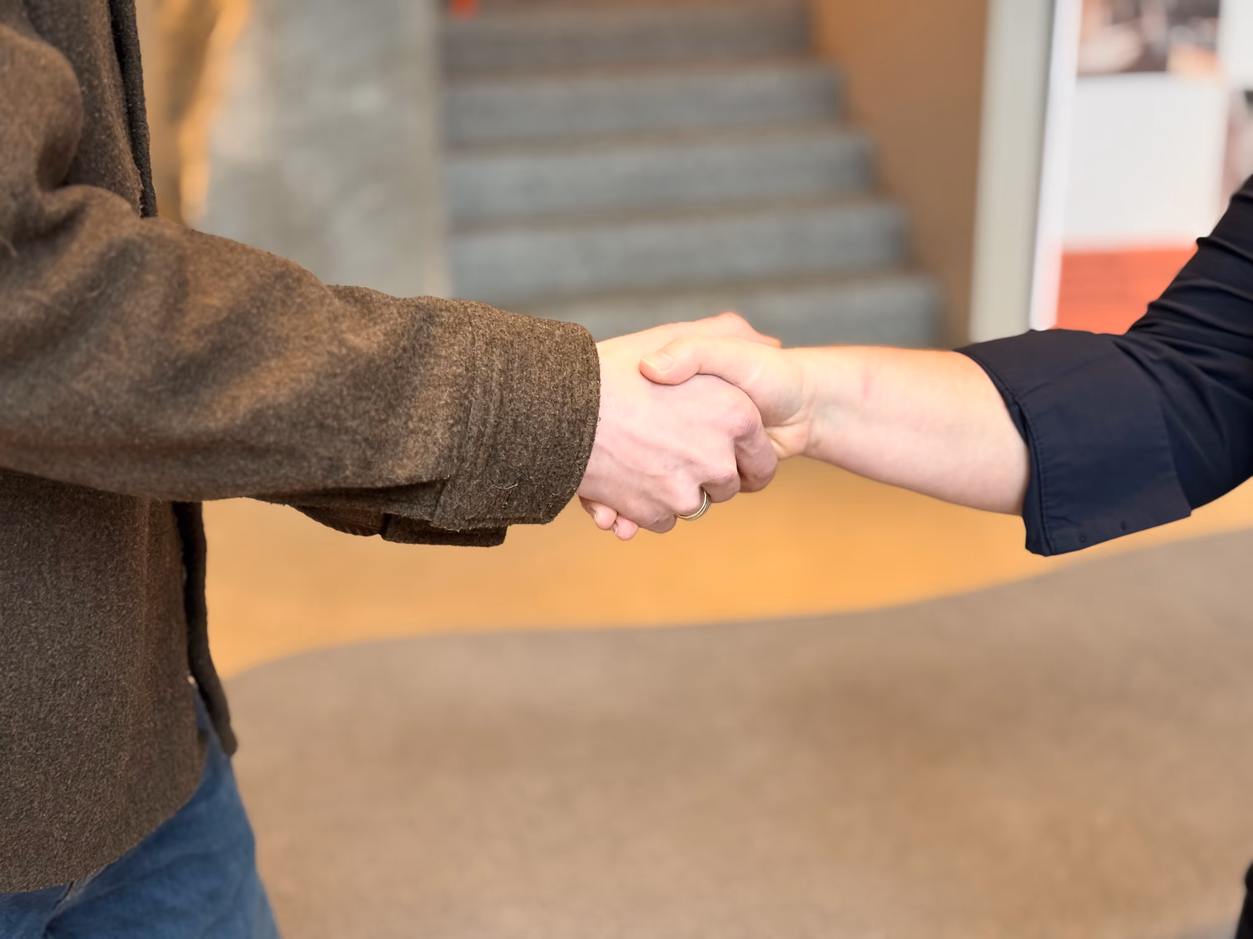 Woman wearing glasses sitting at a desk by a window, writing on a document with a computer monitor and laptop in front of her.