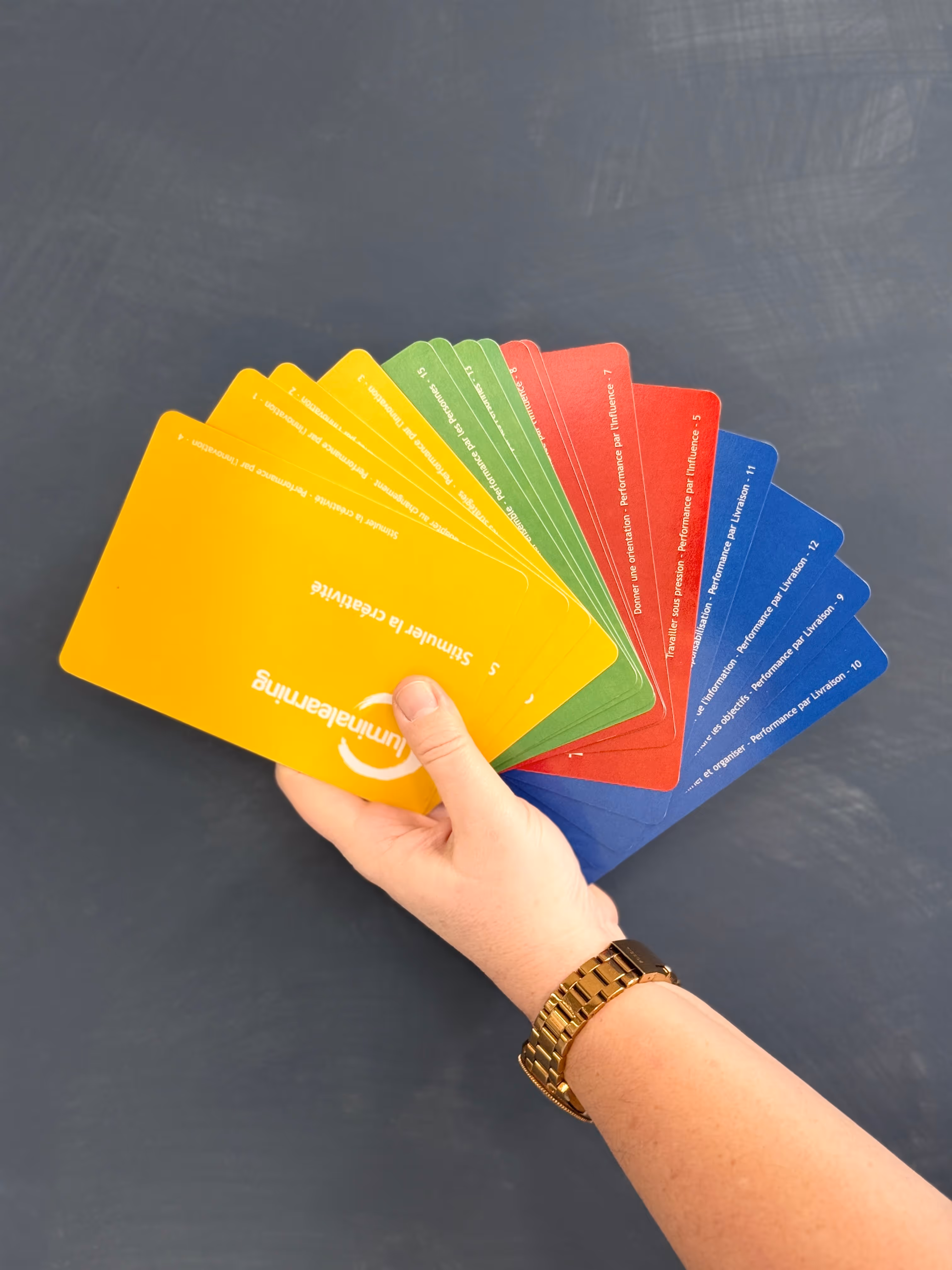 Woman wearing glasses sitting at a desk by a window, writing on a document with a computer monitor and laptop in front of her.