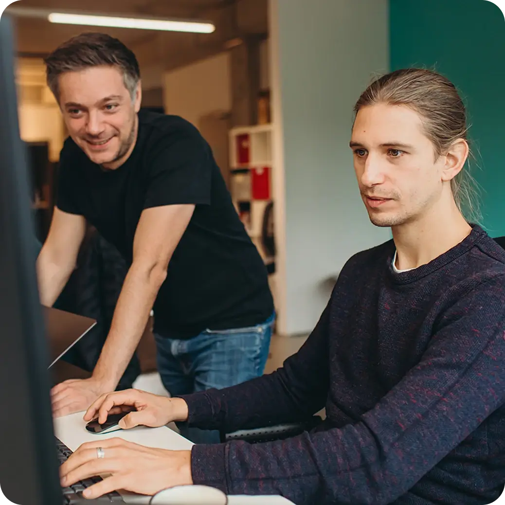 Zwei Männer arbeiten gemeinsam an einem Computer in einem hellen Büro.