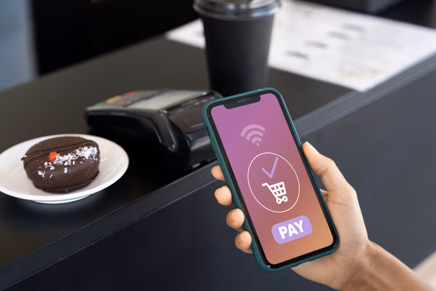 Person holding a smartphone near a payment terminal for contactless mobile payment.