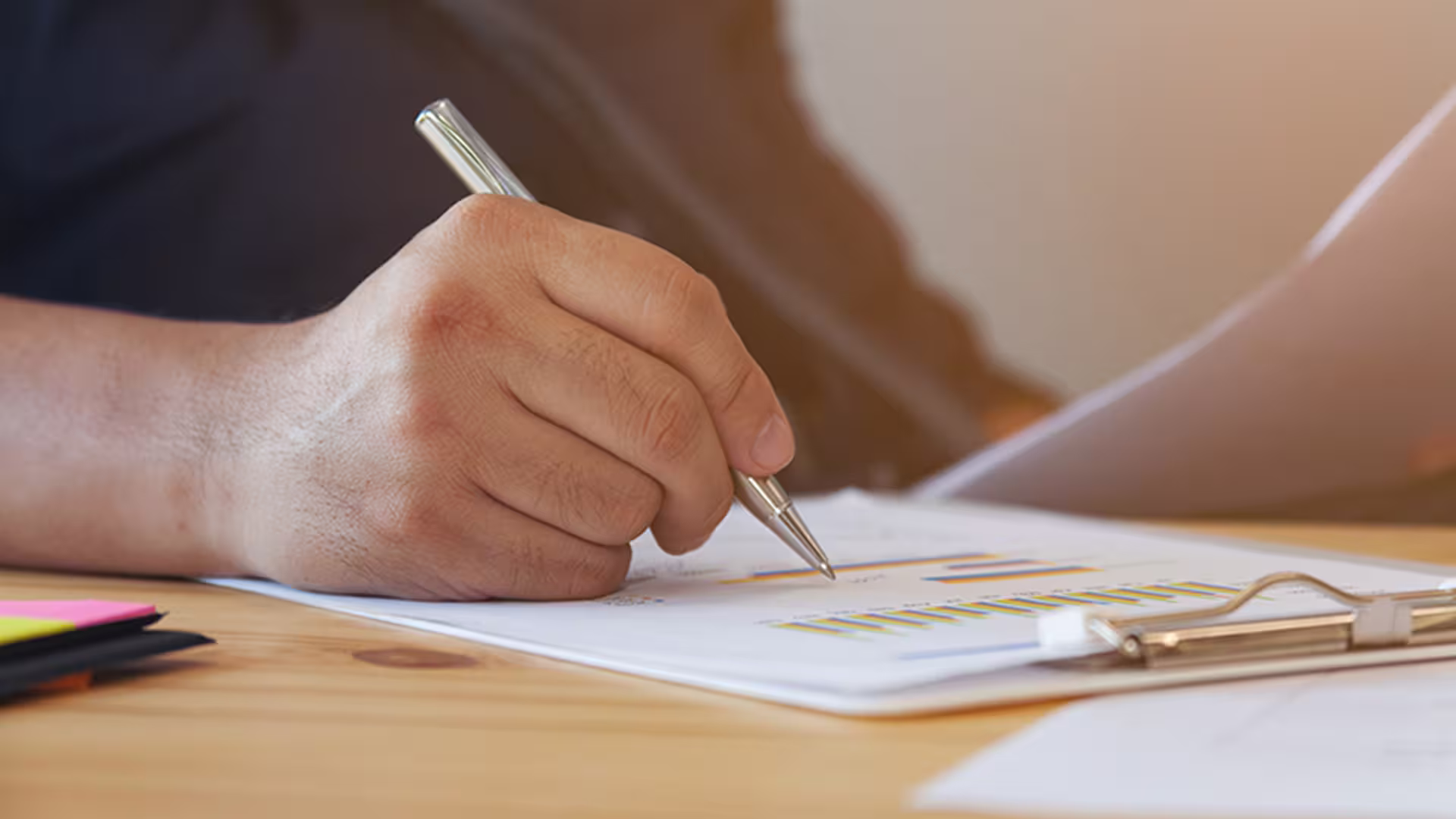 Hand with pen on office reports and charts — writing environmental reports, audits and technical studies