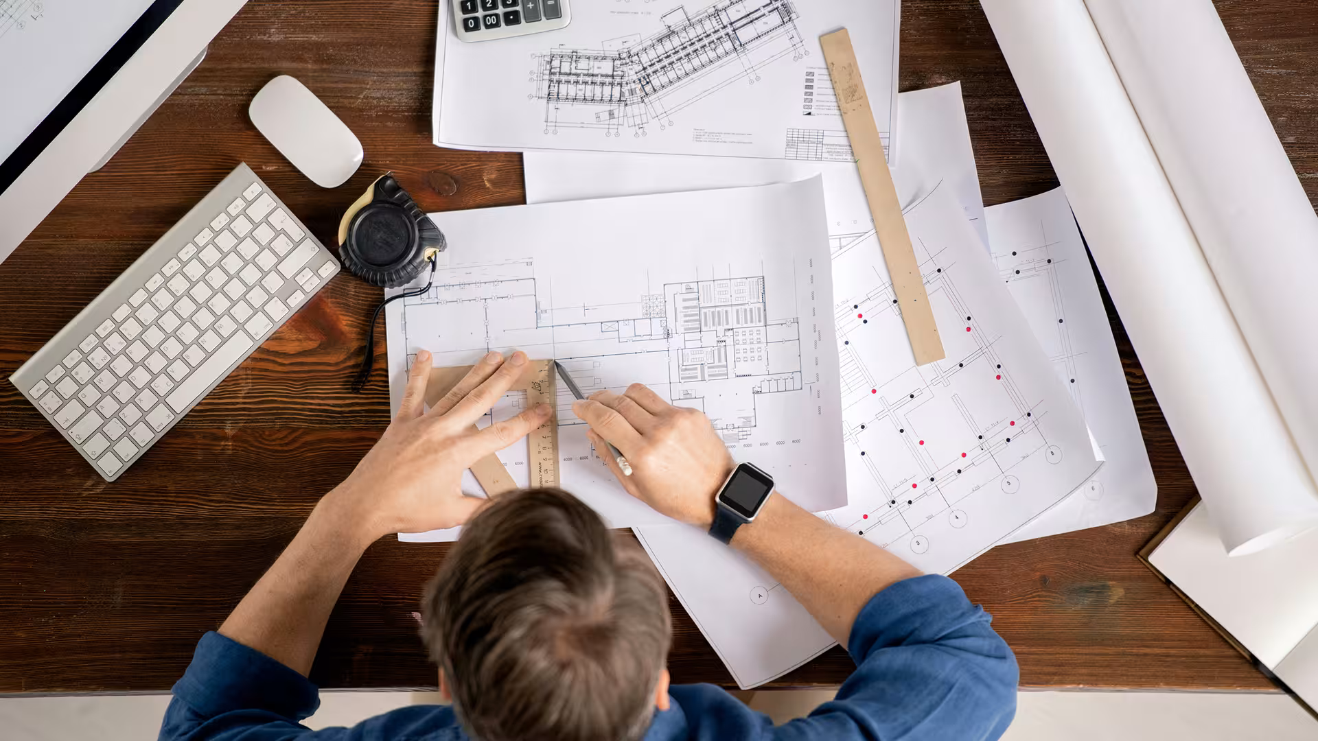 Architecte étudiant des plans techniques étalés sur une table en bois, illustration pour Bâtiment