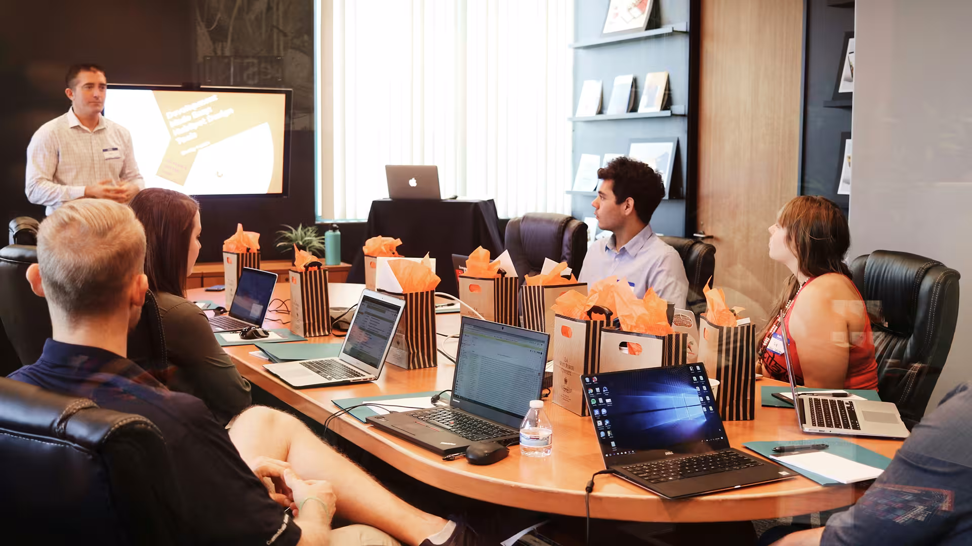 Presenter speaking to a conference room equipped with laptops