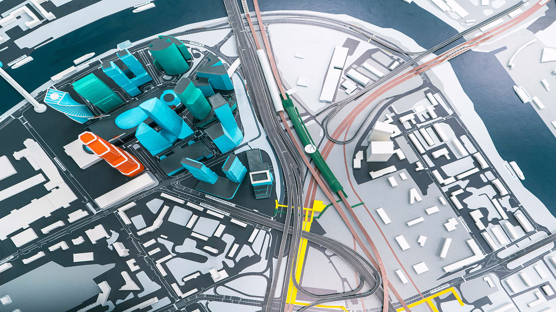 Maquette urbaine en vue aérienne montrant des bâtiments colorés en turquoise et orange, un réseau routier et ferroviaire et un cours d'eau