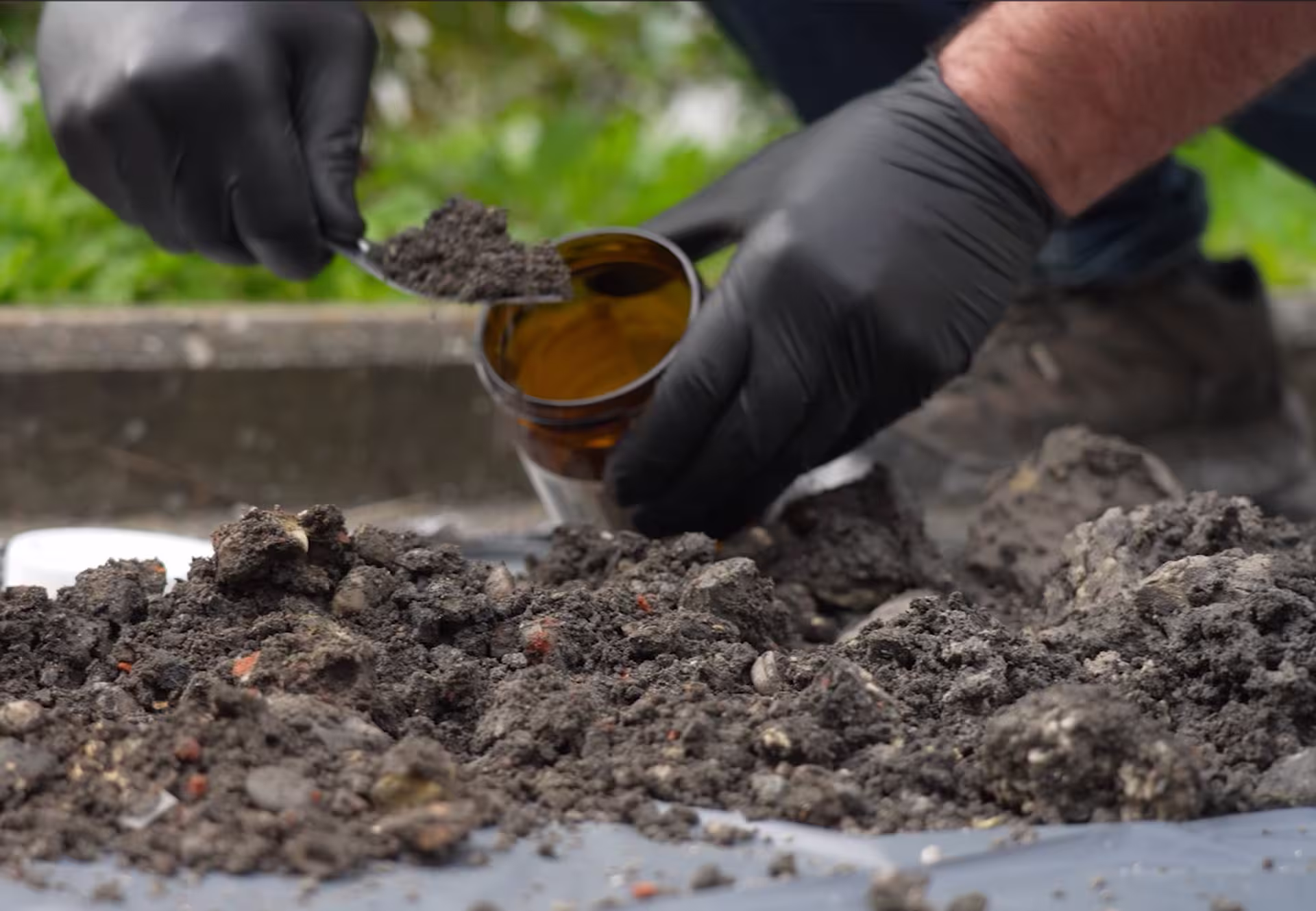 Prélèvement d’un échantillon de sol à l’aide d’une spatule et d’un récipient de laboratoire lors d’une opération d’analyse environnementale.