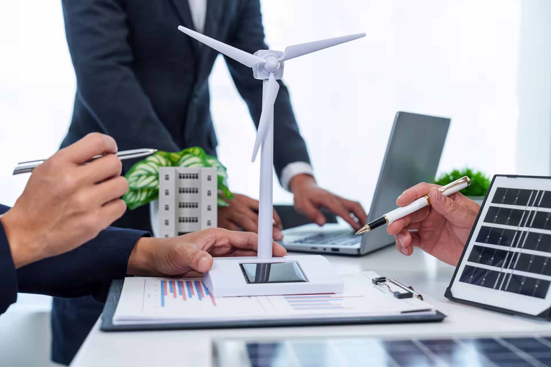 Réunion de travail autour d’un projet d’énergies renouvelables avec une maquette d’éolienne, un panneau solaire et des documents d’analyse.