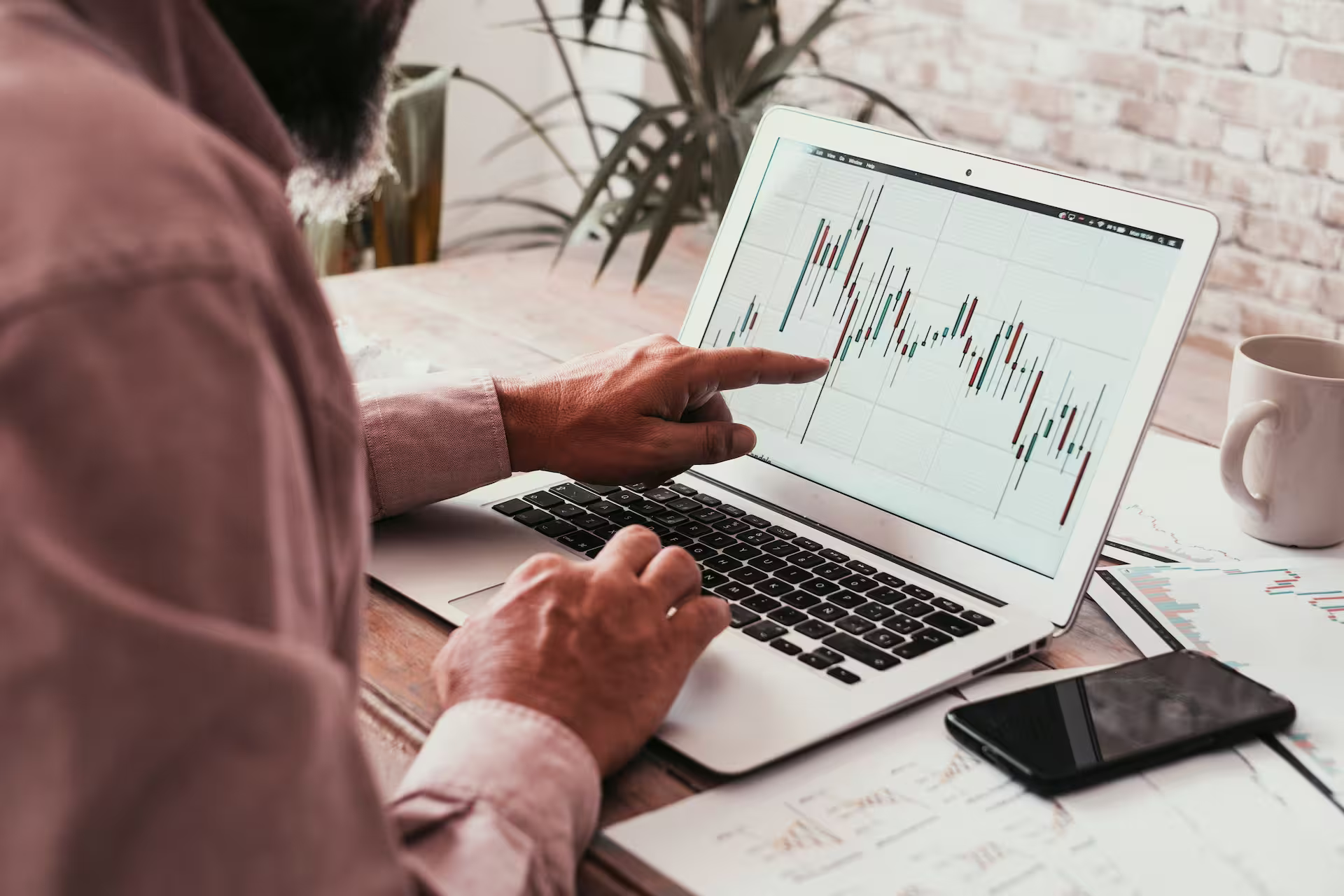 Man pointing his finger at a chart displayed on an open laptop on a desk.