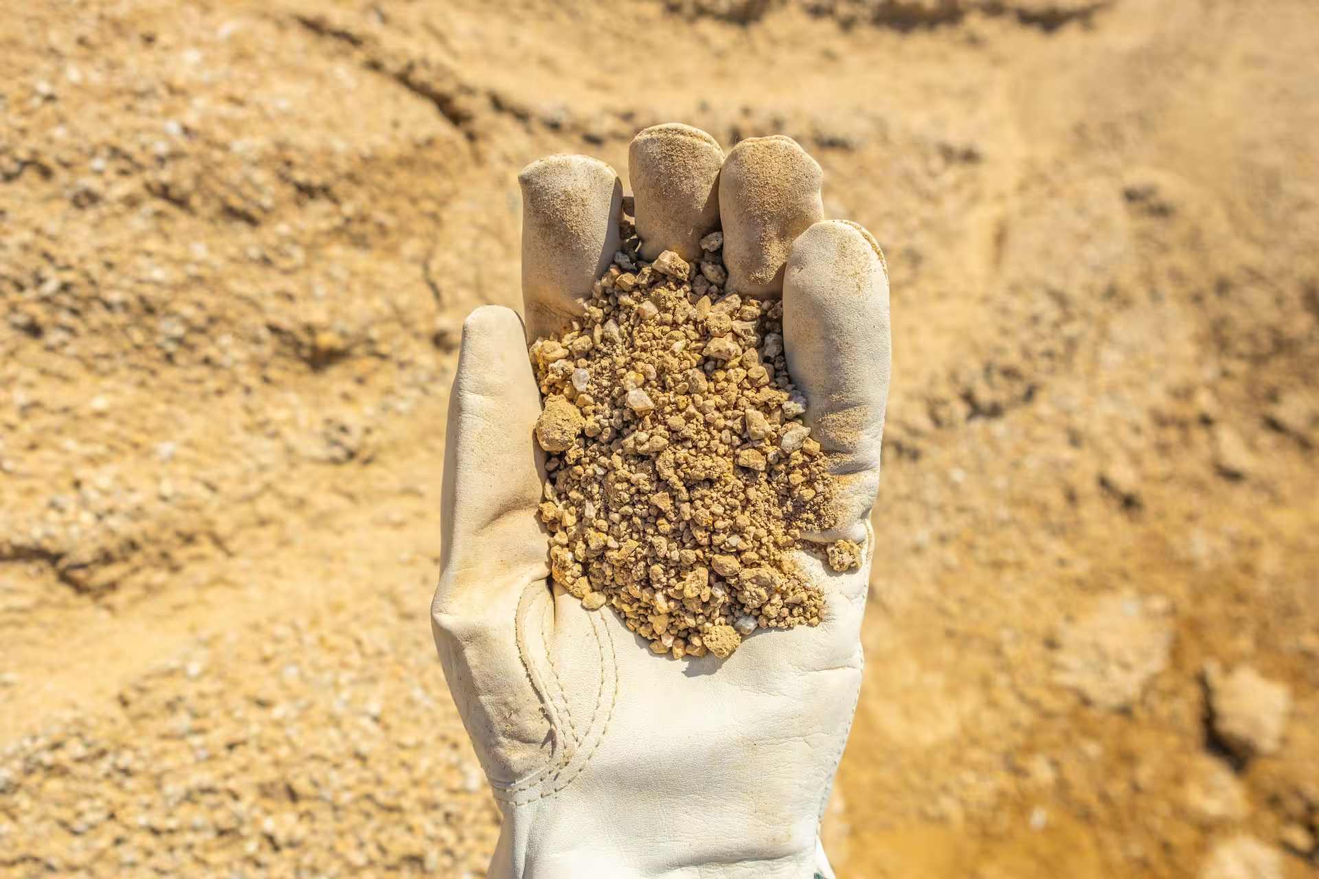Handschoen met een handvol fijn grind en beige aarde op een werf of in een groeve.