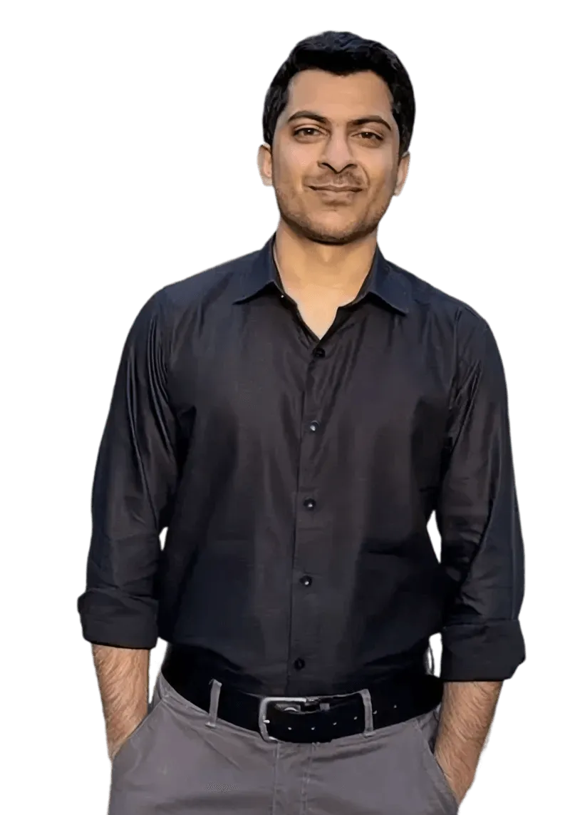 Man wearing a black button-up shirt with rolled-up sleeves and gray pants with a black belt, hands in pockets.