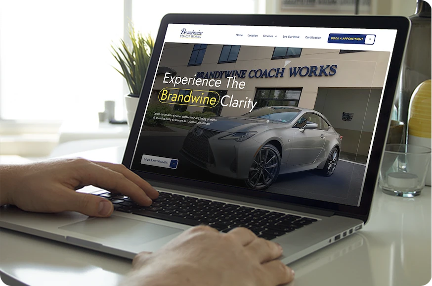 Laptop screen showing Brandywine Coach Works website with a silver sports car and the text 'Experience The Brandwine Clarity'.