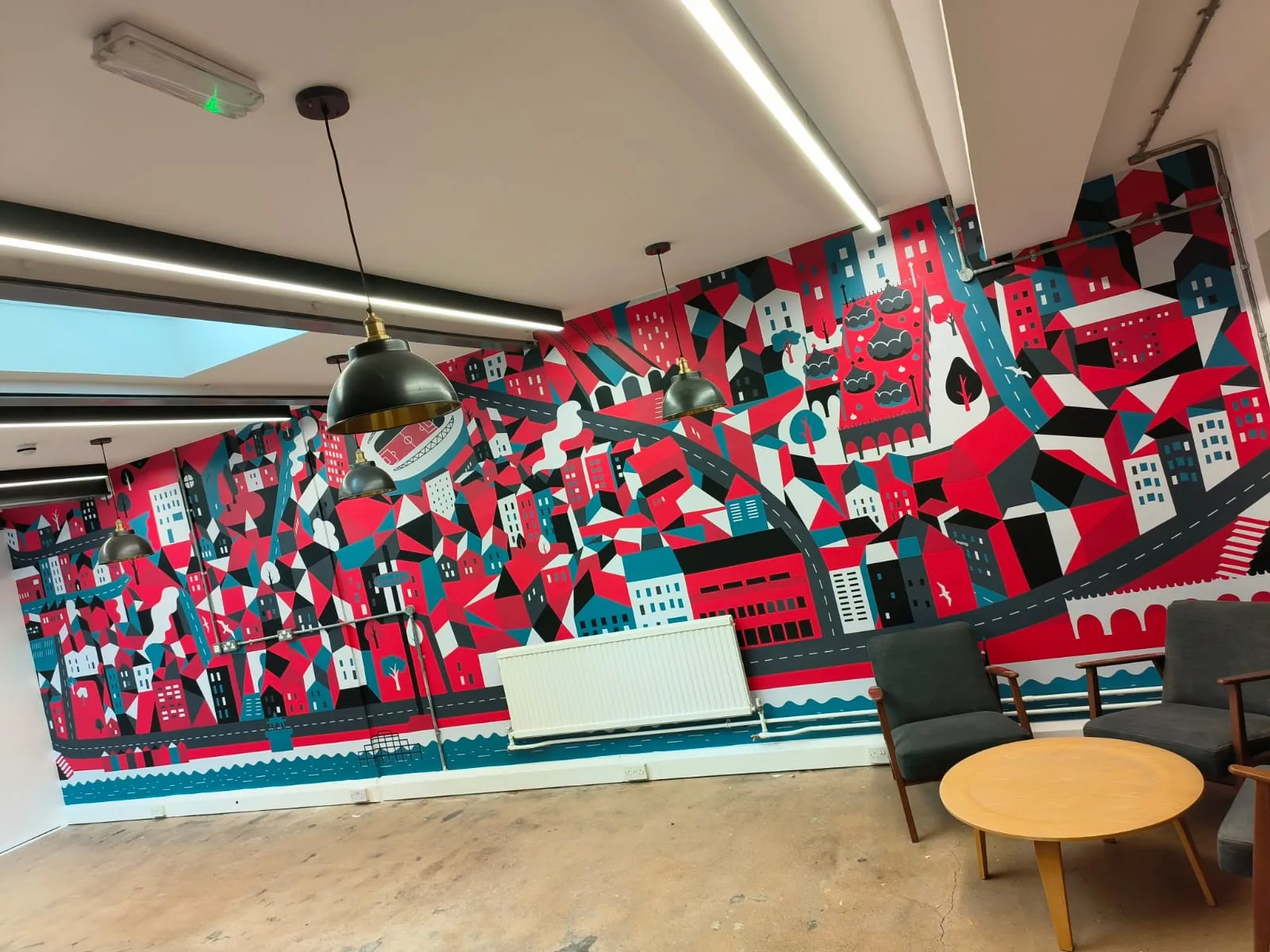 Room with colorful cityscape mural, gray chairs, wooden table, and hanging pendant lights.