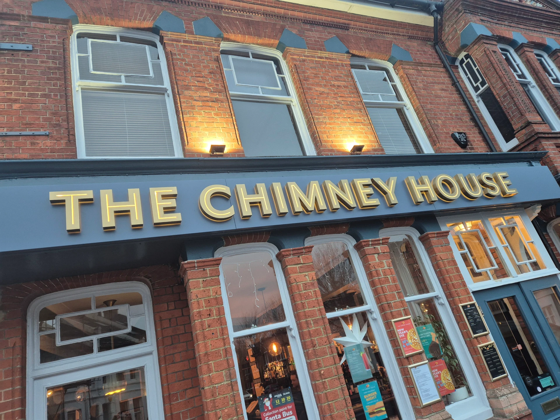 Illuminated The Chimney House pub sign on a brick building.