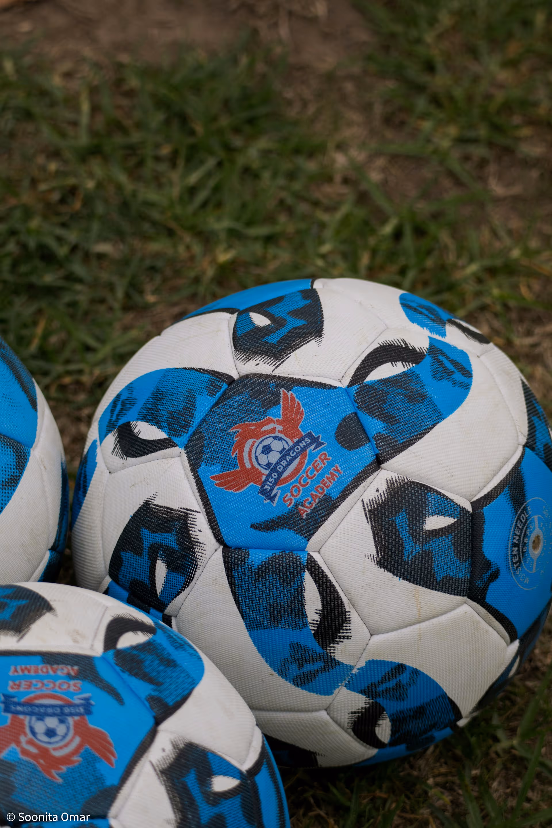 Close-up of blue and white soccer balls on grass with '3150 Dragons Soccer Academy' logo.