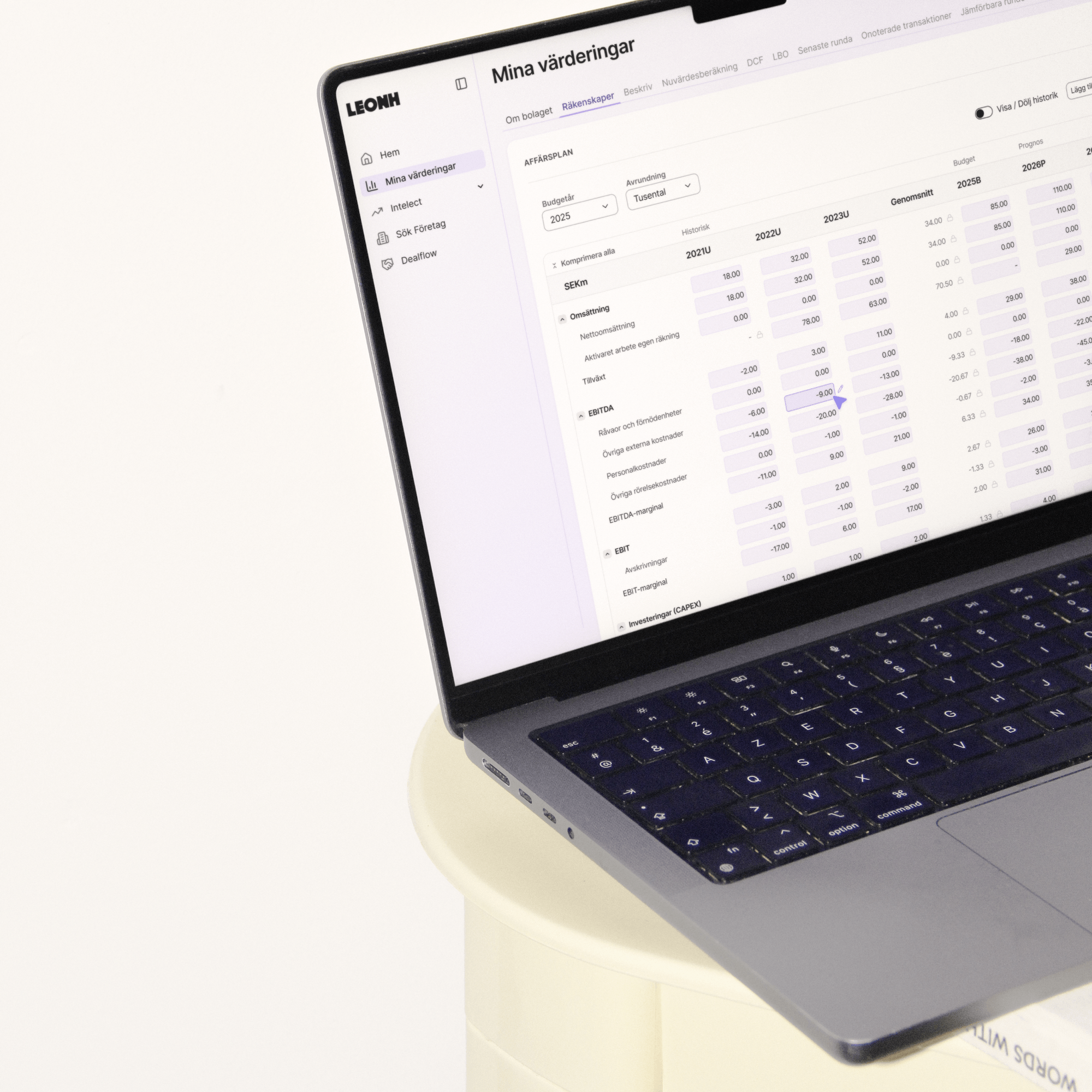 Open laptop on a round white table displaying a Swedish financial planning dashboard with metrics like budget, EBITDA, and EBIT.