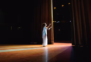 Child on stage pulling back curtain to reveal brightly lit theater.