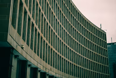 Curved exterior of a multi-story office building with rows of windows and a greenish tint.