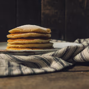 Stack of plain pancakes on a plate next to a striped cloth on a wooden table.