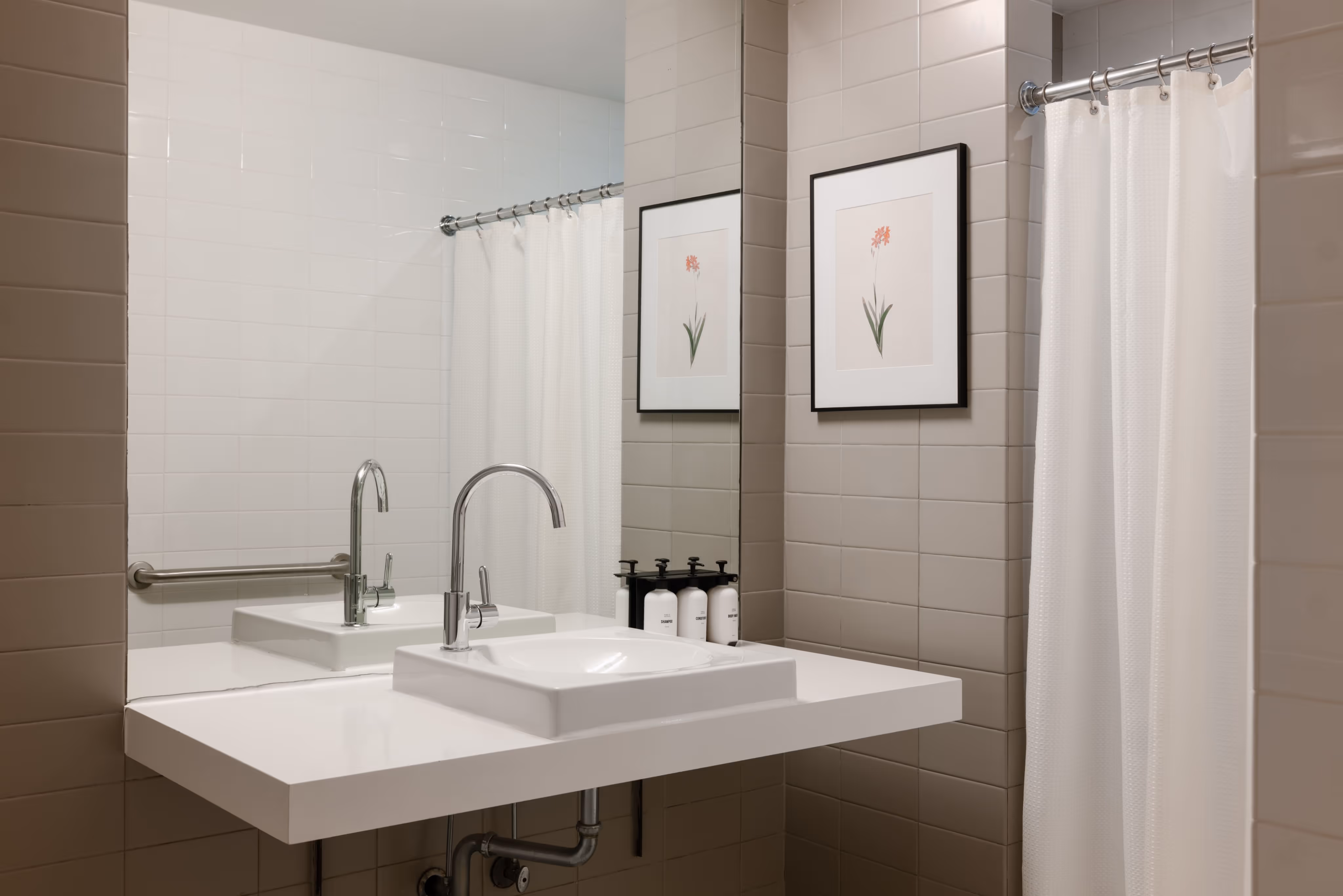 Modern bathroom sink with white countertop, chrome faucet, and a framed floral print on the tiled wall beside a white shower curtain.