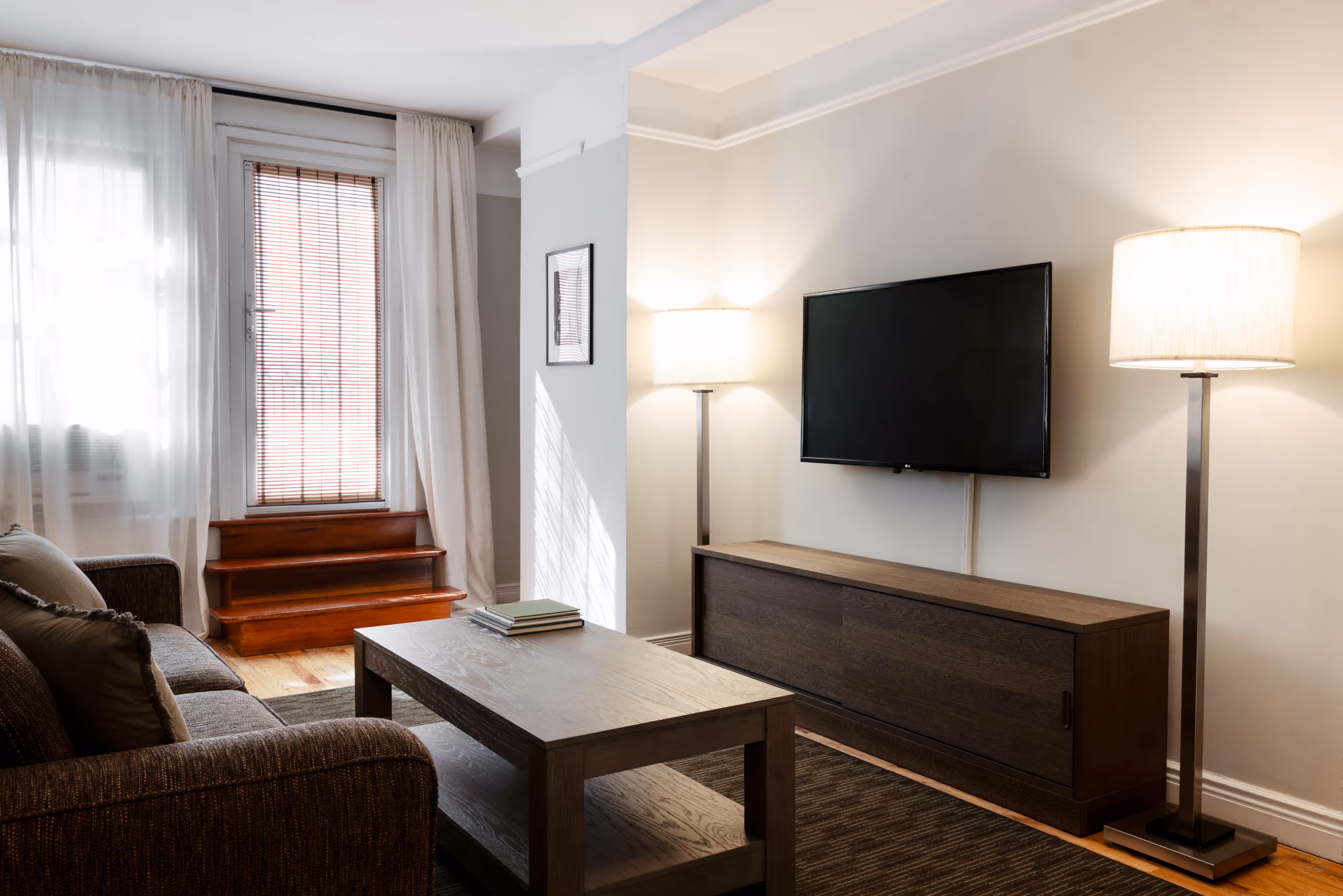 Modern living room with brown sofa, wooden coffee table, flat-screen TV on wooden cabinet, and two floor lamps.