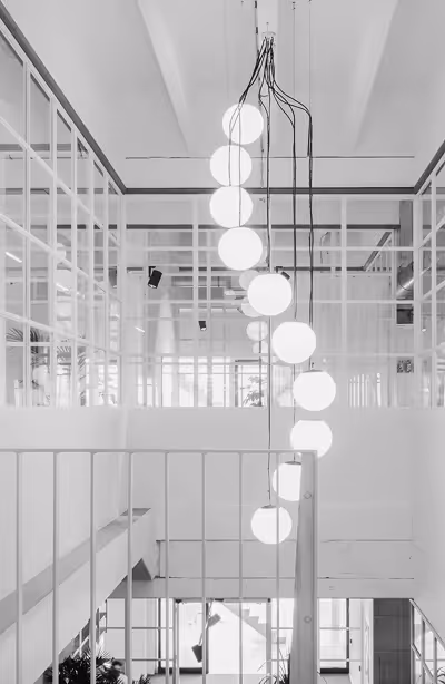 The modern interior of the Brussels office, with a vertical row of round hanging pendant lights in a white, open staircase area featuring glass and metal railings.