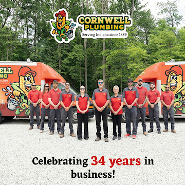 Nine Cornwell Plumbing workers in red shirts posing with plumbing tools and equipment in front of an orange company truck.