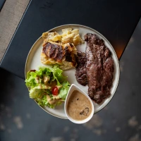 Burger with fried fries on black plate with sauce on the side