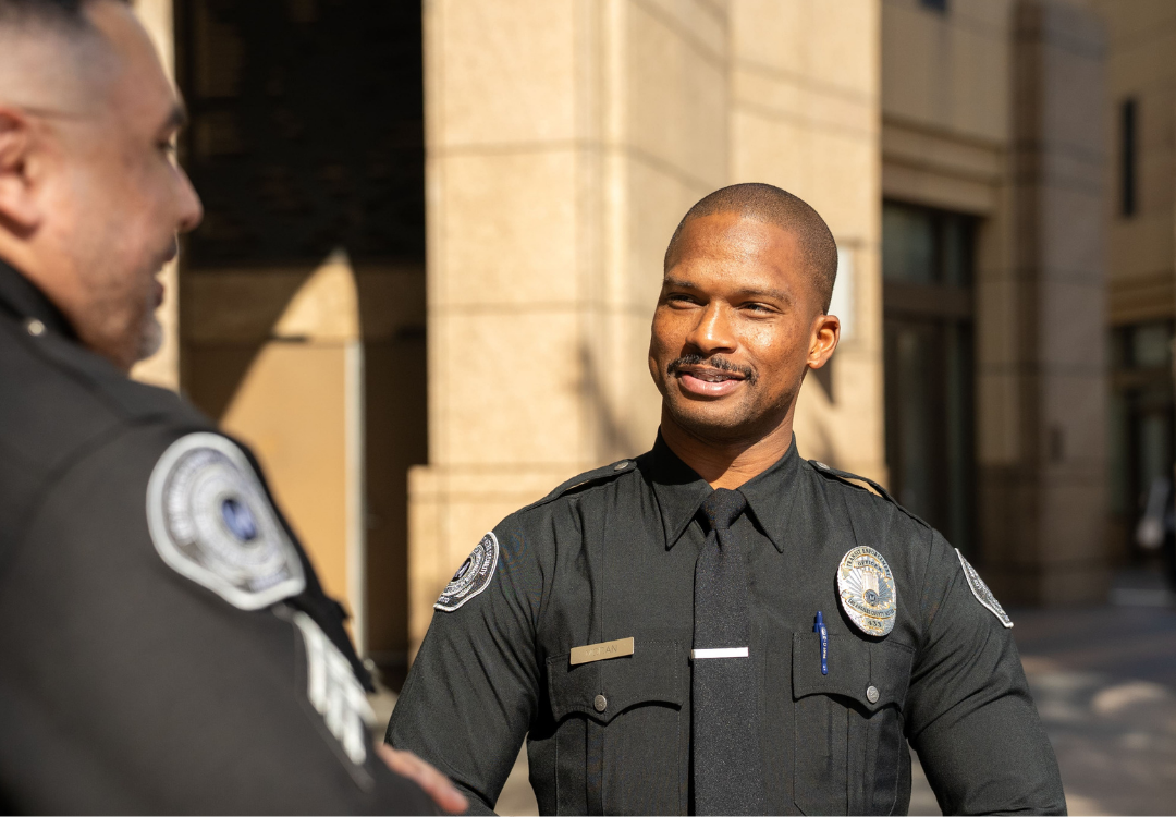 Two police officers in uniform shaking hands outside a building, with one officer smiling.
