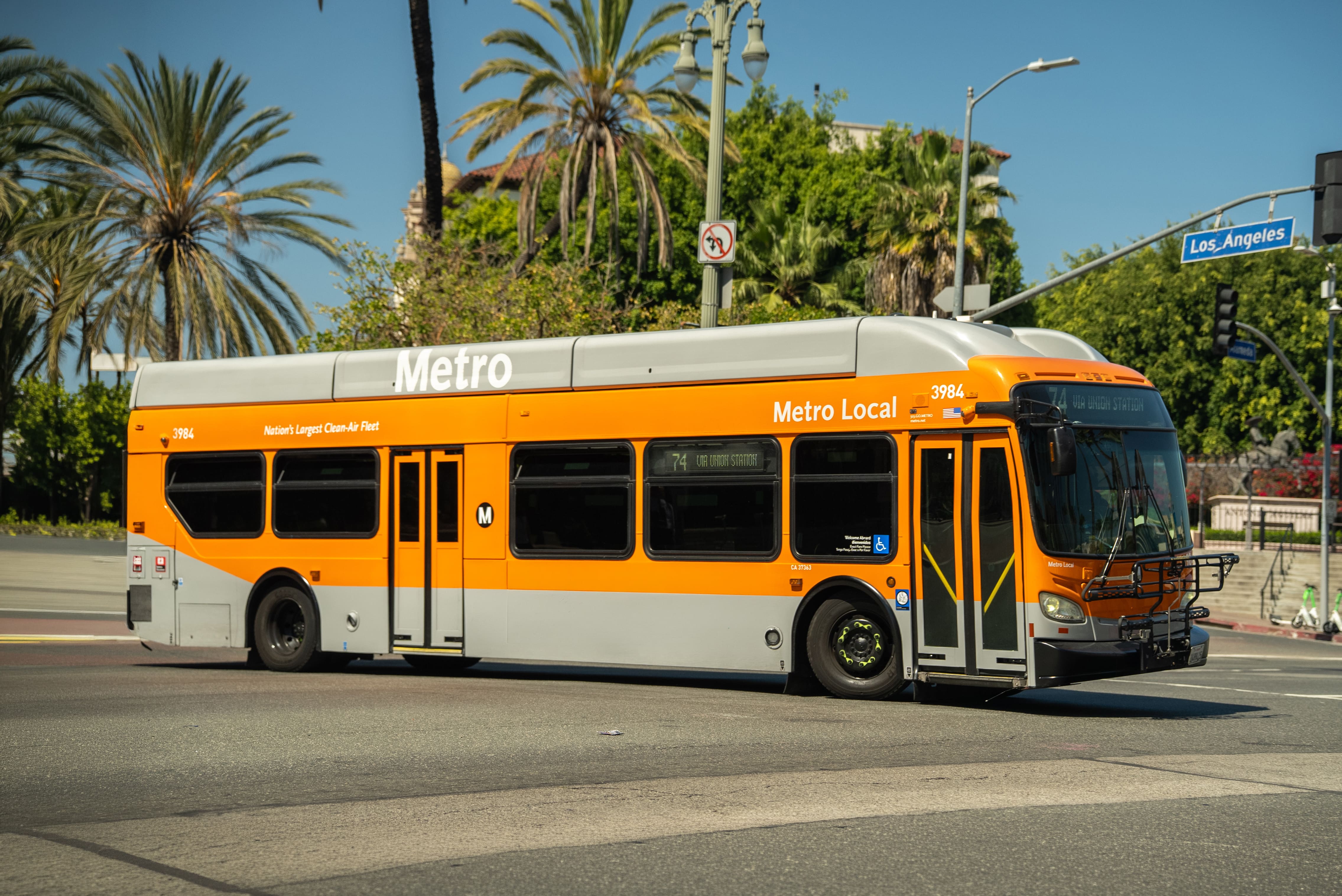 Orange and grey Metro Local bus number 3984 turning at an intersection with palm trees and a Los Angeles street sign in the background.