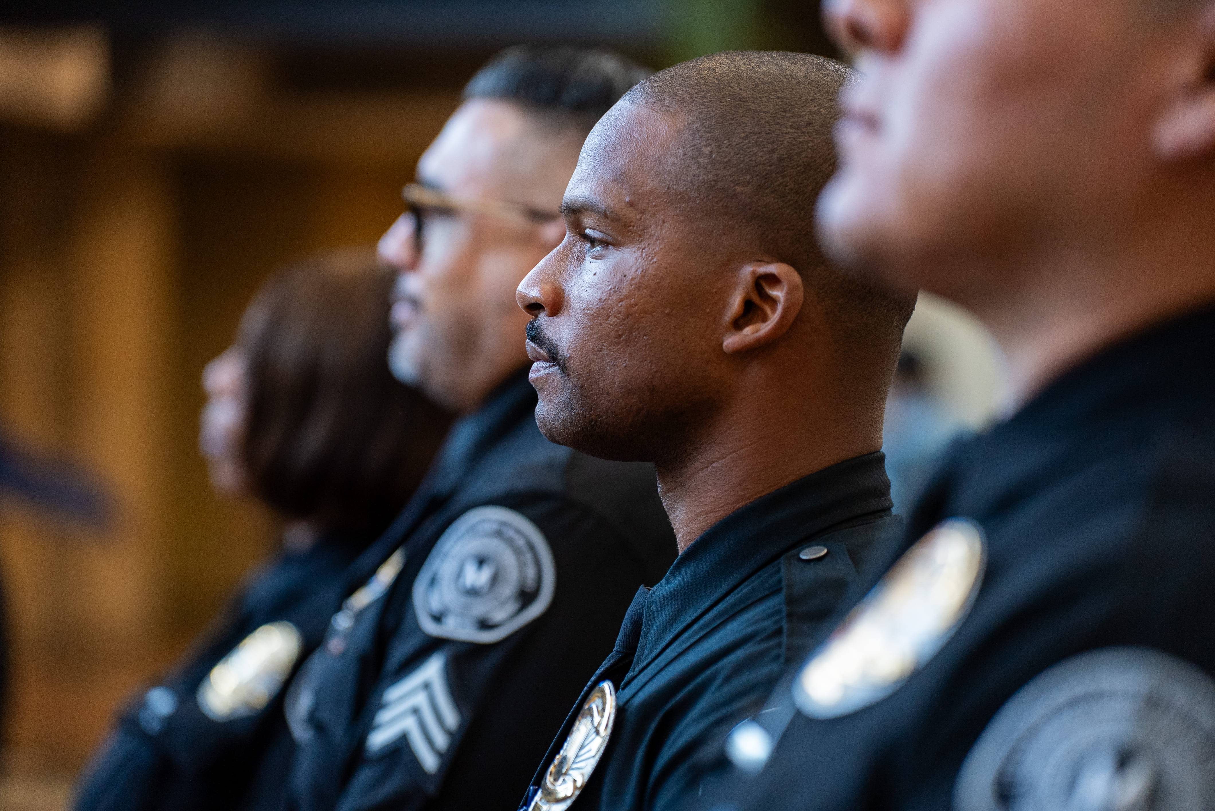 Side view of four serious police officers in uniform standing in a row indoors.
