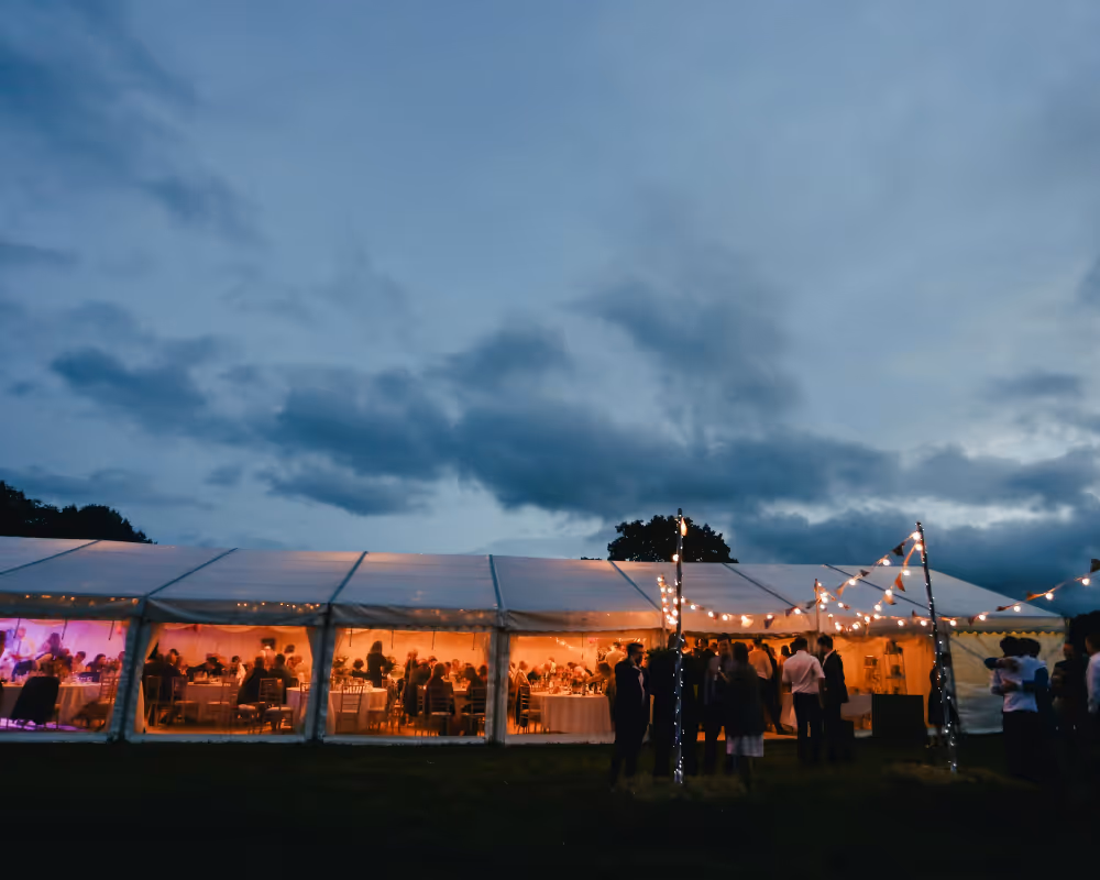 Privat fest i tält med stämningsbelysning, gäster och kvällshimmel i bakgrunden