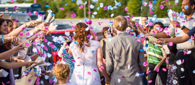 Ett brudpar som går under rosa och blå konfetti på sitt bröllop