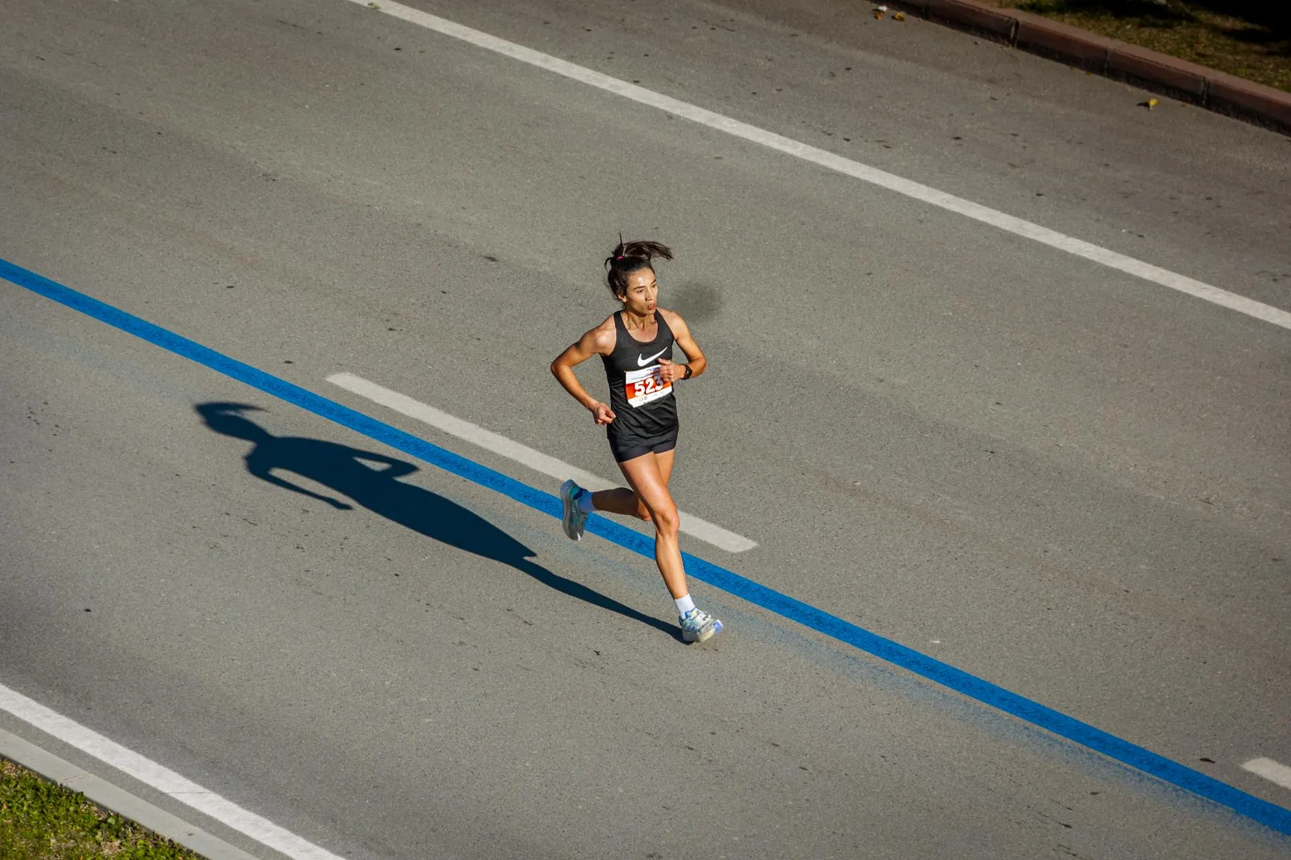 Female runner in black athletic wear running along a road marked with a blue line, casting a shadow on the pavement.
